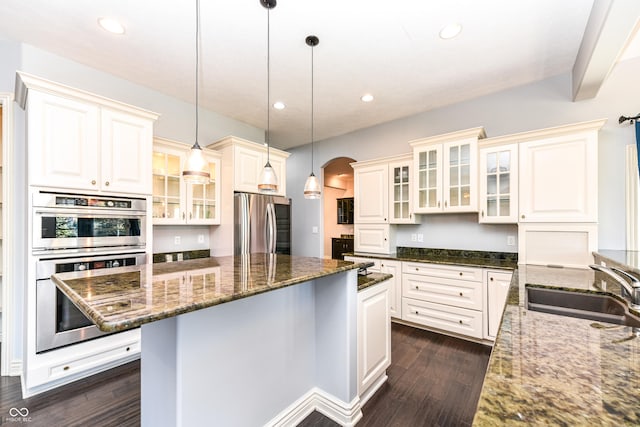 kitchen with dark hardwood / wood-style flooring, stainless steel appliances, hanging light fixtures, and dark stone counters