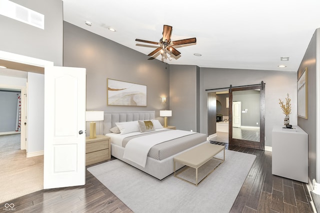 bedroom with ceiling fan, a barn door, dark hardwood / wood-style flooring, and high vaulted ceiling