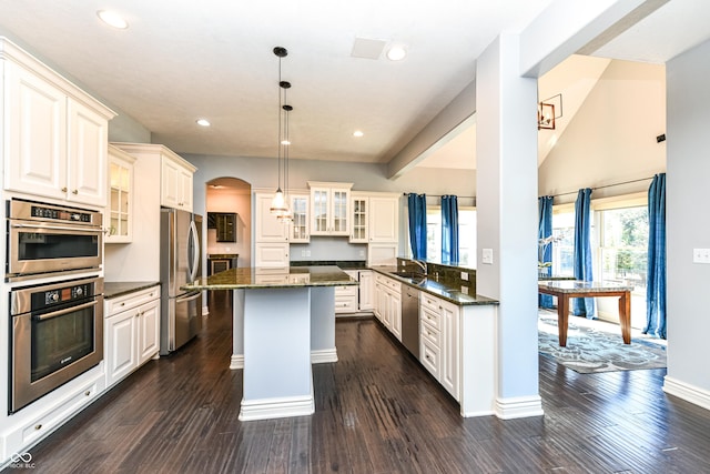 kitchen with stainless steel appliances, a kitchen island, hanging light fixtures, and dark wood-type flooring