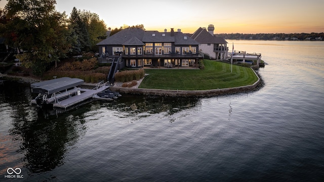 back house at dusk featuring a water view and a lawn