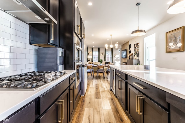 kitchen with wall chimney range hood, stainless steel gas cooktop, pendant lighting, light hardwood / wood-style floors, and tasteful backsplash