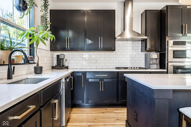 kitchen featuring wall chimney range hood, backsplash, appliances with stainless steel finishes, light hardwood / wood-style flooring, and sink