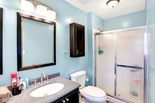 bathroom with vanity, a textured ceiling, toilet, and a shower with shower door