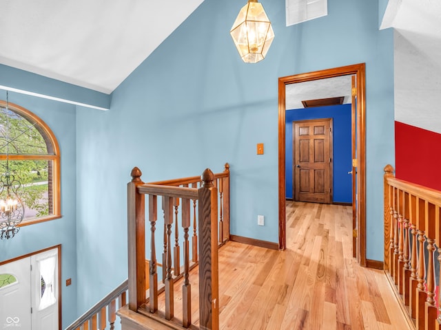 hallway featuring light wood-style floors, an upstairs landing, a notable chandelier, high vaulted ceiling, and visible vents
