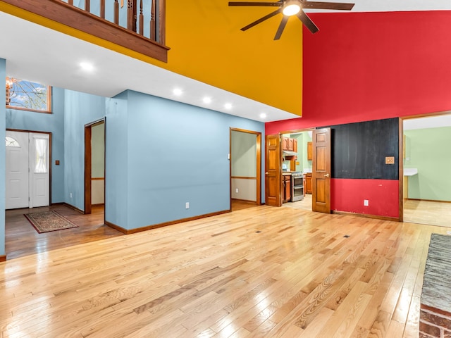 unfurnished living room with ceiling fan, baseboards, light wood finished floors, and a high ceiling
