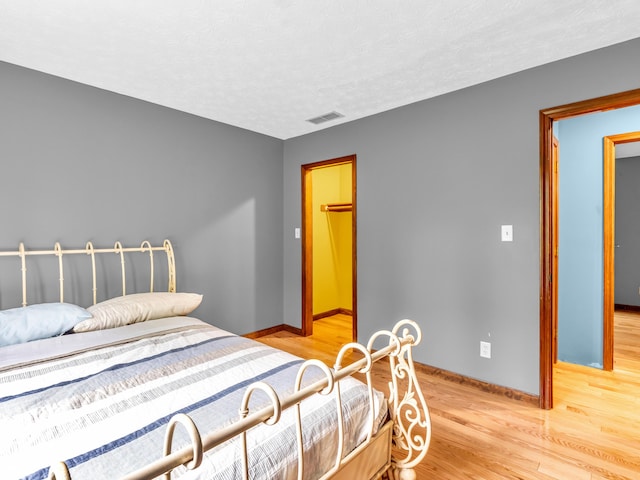 bedroom featuring baseboards, visible vents, light wood-type flooring, and a textured ceiling