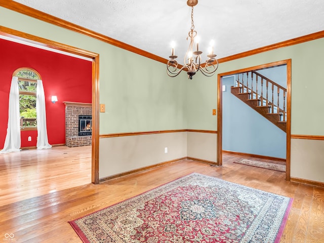 interior space with an inviting chandelier, stairway, wood-type flooring, a brick fireplace, and crown molding