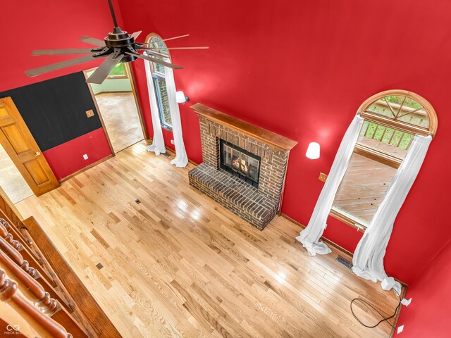 unfurnished living room with a towering ceiling, ceiling fan, wood finished floors, and a fireplace