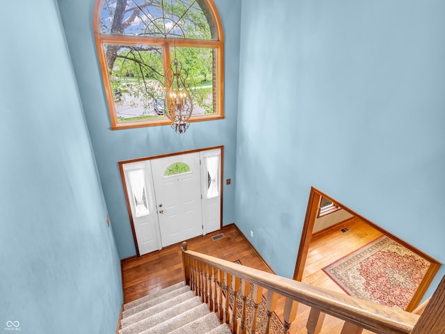 entrance foyer featuring stairway, a chandelier, visible vents, wood-type flooring, and a high ceiling