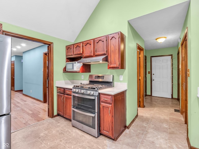 kitchen with under cabinet range hood, light countertops, baseboards, appliances with stainless steel finishes, and lofted ceiling
