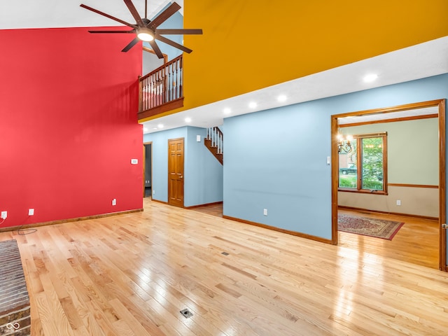 unfurnished living room with wood finished floors, ceiling fan, baseboards, stairway, and a high ceiling
