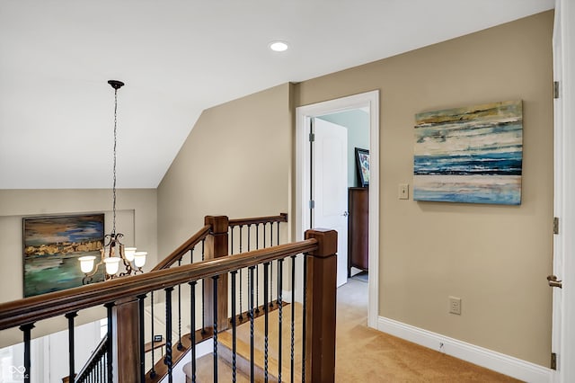 corridor with baseboards, light colored carpet, lofted ceiling, an inviting chandelier, and an upstairs landing