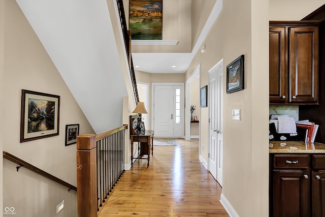 hall with light wood-style floors, baseboards, and an upstairs landing