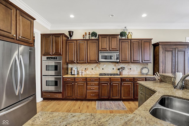 kitchen with light wood finished floors, tasteful backsplash, ornamental molding, stainless steel appliances, and a sink