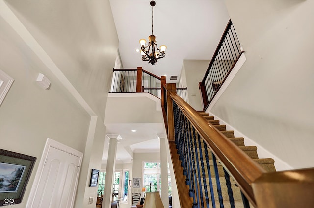 stairs with a notable chandelier, crown molding, a towering ceiling, and ornate columns