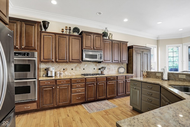 kitchen featuring light stone counters, stainless steel appliances, decorative backsplash, light wood-style floors, and ornamental molding