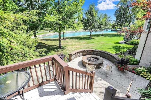 wooden terrace with an outdoor fire pit, a water view, and a lawn