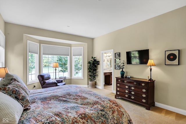 bedroom featuring baseboards, connected bathroom, and light colored carpet