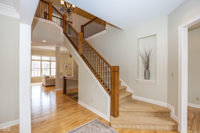 stairs with an inviting chandelier, a high ceiling, baseboards, and wood finished floors