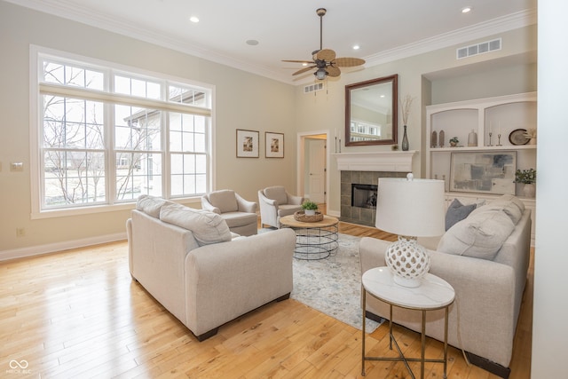 living room featuring light wood finished floors, baseboards, visible vents, a tile fireplace, and crown molding