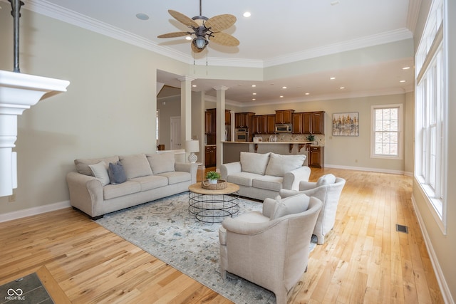 living area featuring ornamental molding, visible vents, decorative columns, and light wood finished floors