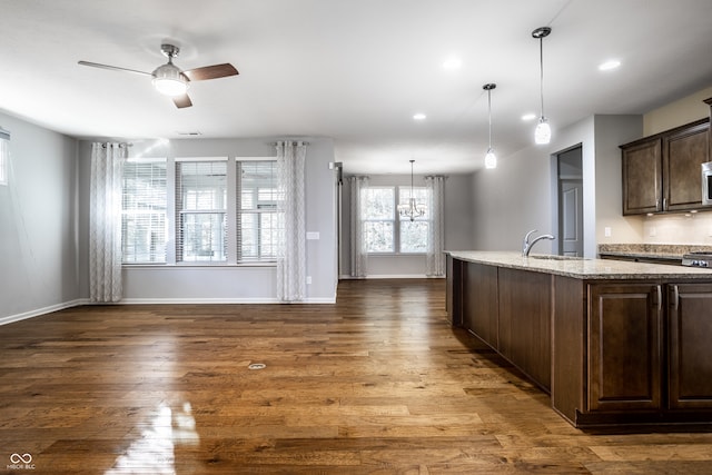 kitchen featuring light stone countertops, sink, dark hardwood / wood-style flooring, dark brown cabinetry, and pendant lighting