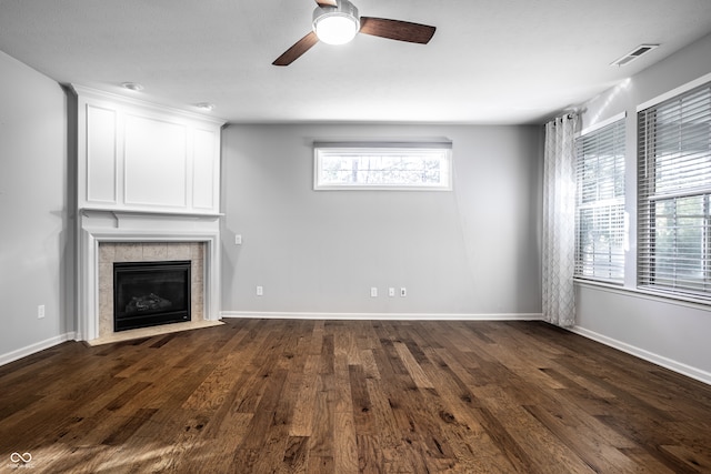 unfurnished living room with a tiled fireplace, dark hardwood / wood-style floors, and ceiling fan