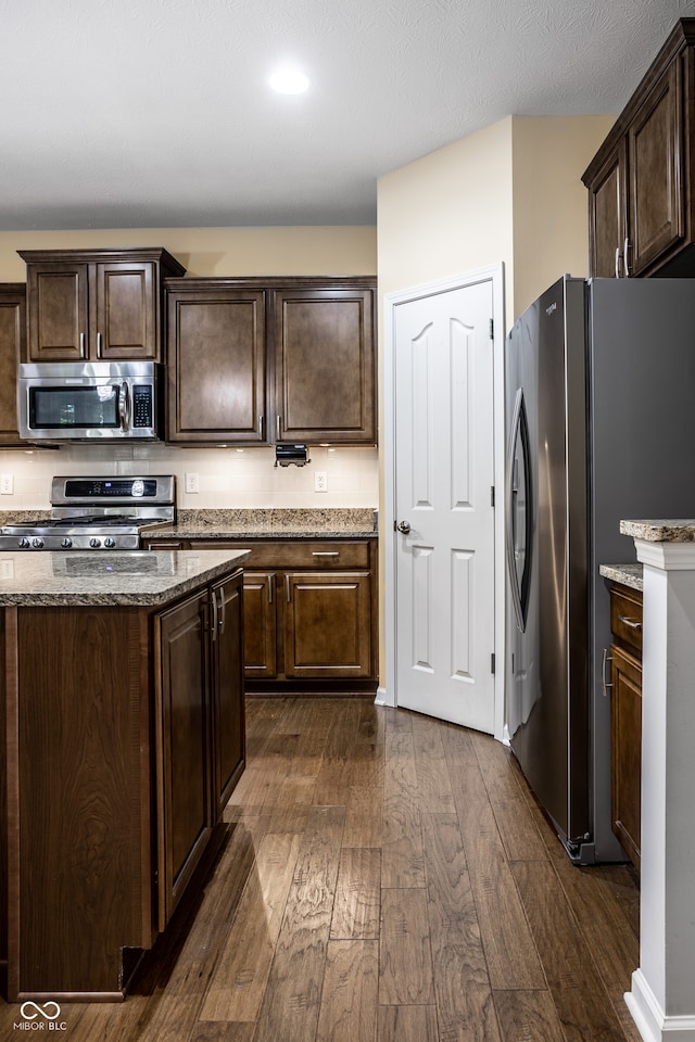 kitchen with appliances with stainless steel finishes, dark brown cabinetry, light stone countertops, and dark hardwood / wood-style flooring