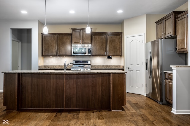 kitchen with appliances with stainless steel finishes, a kitchen island with sink, hanging light fixtures, and dark hardwood / wood-style flooring