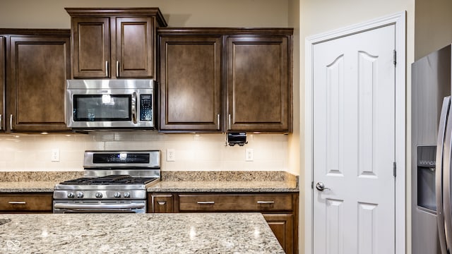 kitchen with appliances with stainless steel finishes, decorative backsplash, dark brown cabinetry, and light stone counters