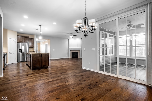 kitchen featuring appliances with stainless steel finishes, a kitchen island with sink, dark wood-type flooring, ceiling fan with notable chandelier, and decorative light fixtures