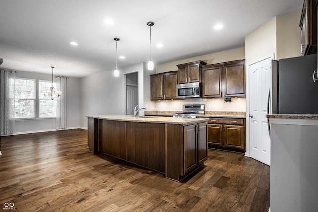 kitchen with dark brown cabinets, appliances with stainless steel finishes, a kitchen island with sink, dark wood-type flooring, and decorative light fixtures