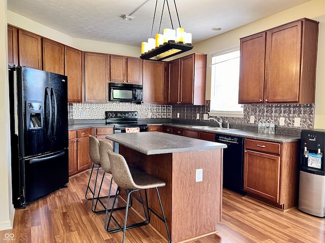 kitchen with black appliances, sink, light wood-type flooring, a kitchen island, and a breakfast bar area