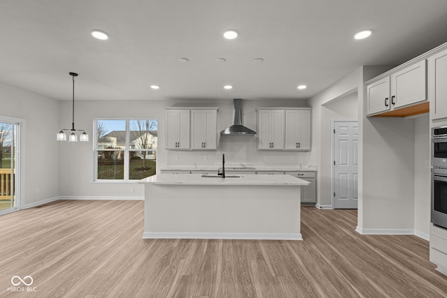 kitchen with pendant lighting, a healthy amount of sunlight, wall chimney range hood, and light hardwood / wood-style flooring