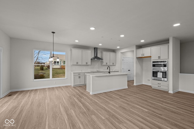 kitchen featuring white cabinetry, hanging light fixtures, double oven, and wall chimney range hood