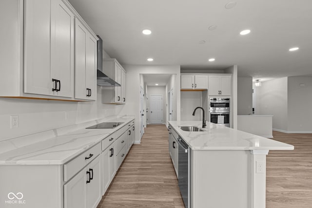 kitchen featuring black electric cooktop, double oven, sink, white cabinetry, and an island with sink