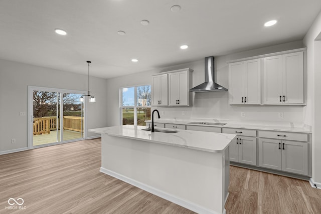 kitchen with black electric stovetop, an island with sink, wall chimney exhaust hood, and sink