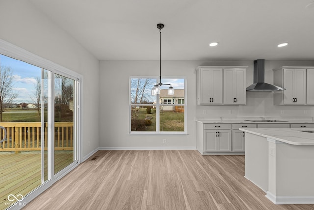 kitchen featuring white cabinets, black electric stovetop, decorative light fixtures, and wall chimney range hood