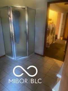 bathroom featuring an enclosed shower, tile patterned floors, and washing machine and clothes dryer