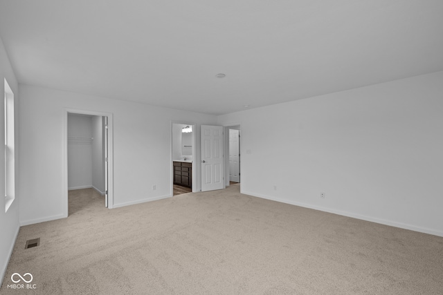 unfurnished bedroom with light colored carpet, connected bathroom, a closet, and a walk in closet