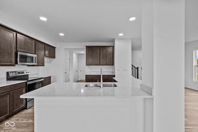 kitchen featuring light stone counters, sink, dark brown cabinets, light wood-type flooring, and appliances with stainless steel finishes