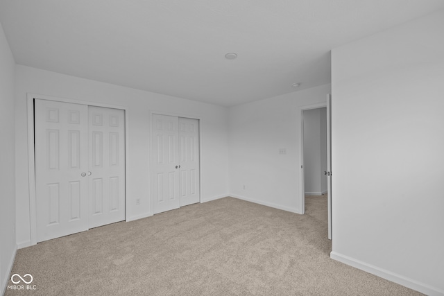 unfurnished bedroom featuring multiple closets and light colored carpet