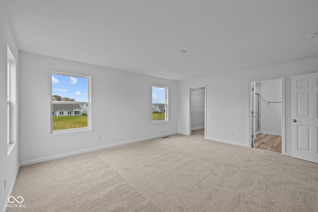 unfurnished bedroom with a spacious closet, light colored carpet, and a closet