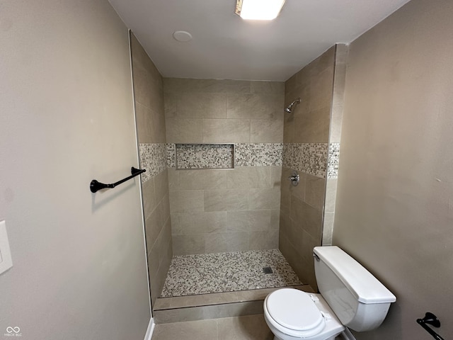 bathroom with tiled shower, toilet, and tile patterned flooring