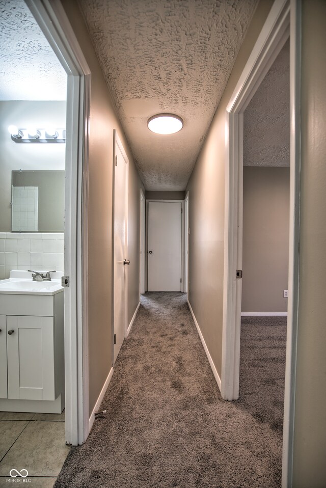 corridor featuring sink, carpet floors, and a textured ceiling