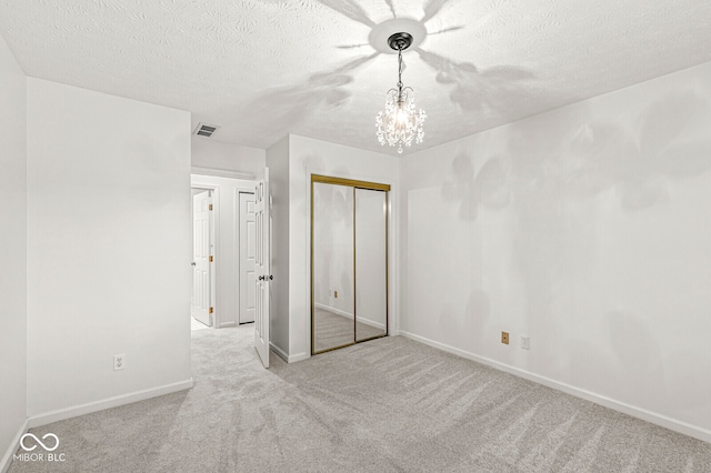 unfurnished bedroom featuring light carpet, a textured ceiling, a chandelier, and a closet