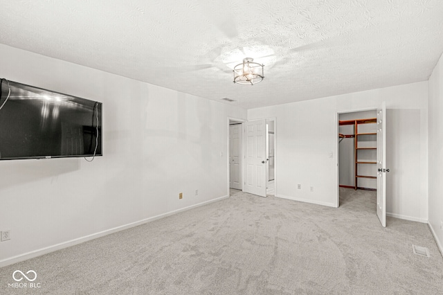 unfurnished bedroom with light carpet, a walk in closet, a closet, and a textured ceiling