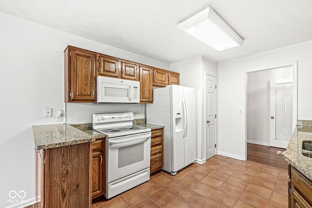 kitchen featuring white appliances, light stone countertops, a textured ceiling, and light tile patterned floors