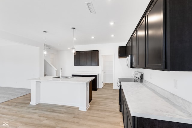 kitchen featuring pendant lighting, sink, stainless steel range with electric cooktop, light hardwood / wood-style floors, and a center island with sink