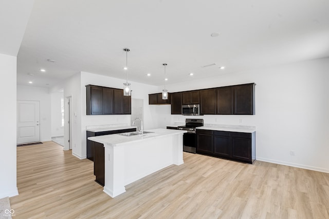 kitchen with sink, hanging light fixtures, a center island with sink, light wood-type flooring, and appliances with stainless steel finishes